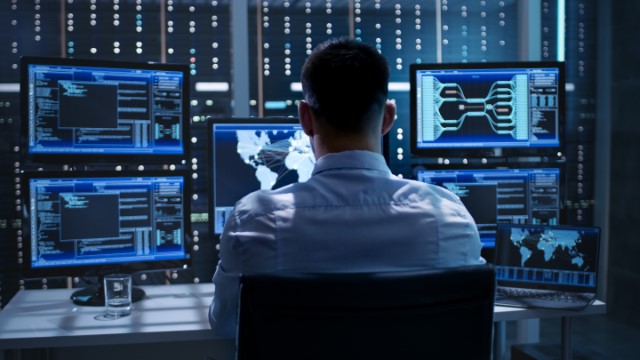 cyber professional sitting at desk with multiple moniors watcing them carefully